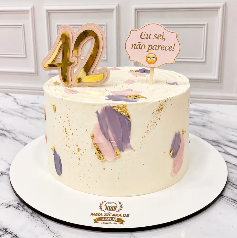 Bolo com pinceladas lilás e rosa, folha de ouro e topo de 42 anos